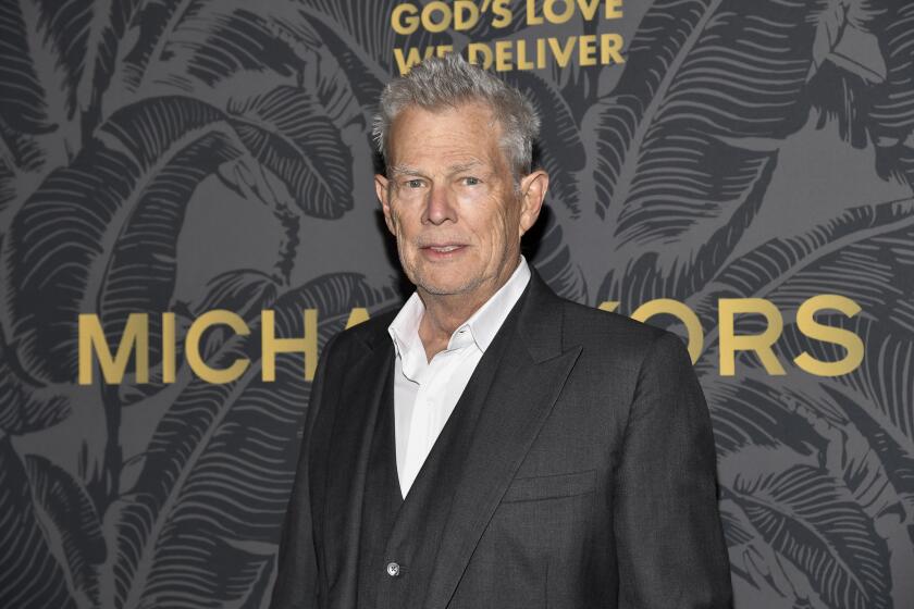 David Foster in a suit with no tie standing behind a dark background