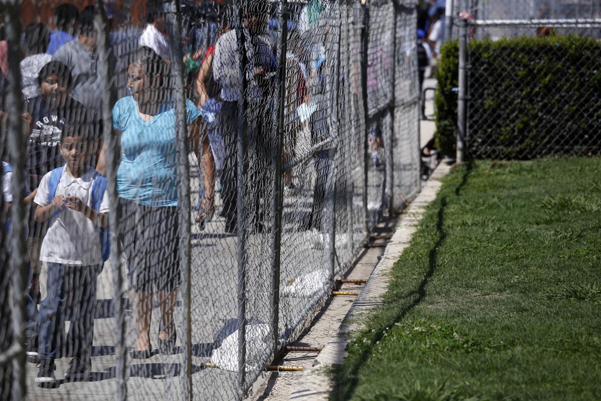 Parents who are picking up their kids after school walk by temporary fencing at Rowan Avenue Elementary in East Los Angeles on Aug. 18.
