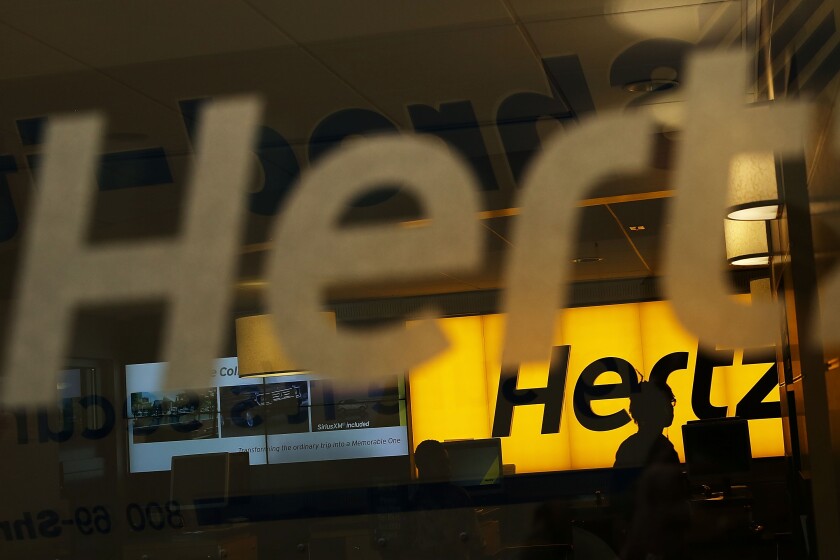 A window opens into an office with the word "Hertz" on the back wall.