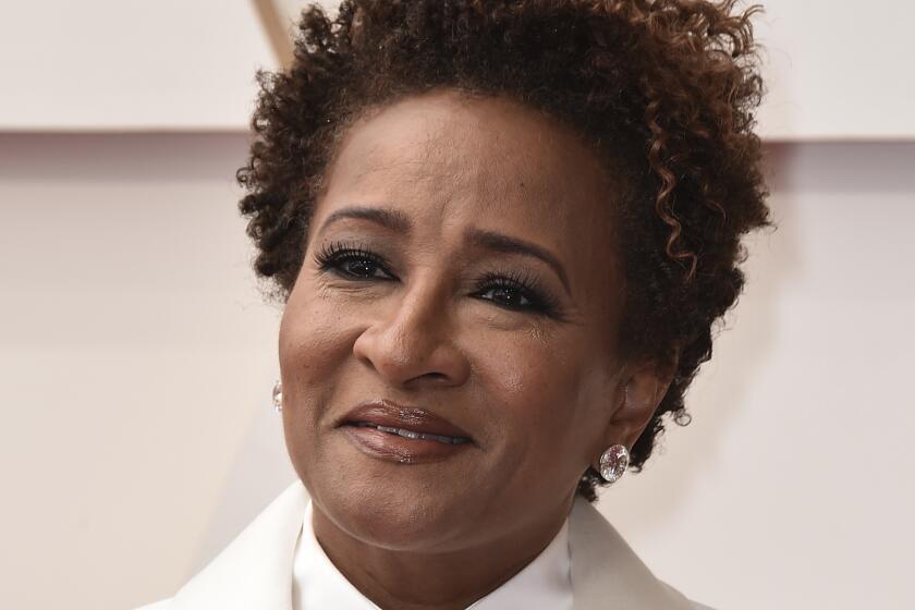 A Black woman in a white tuxedo poses on a red carpet