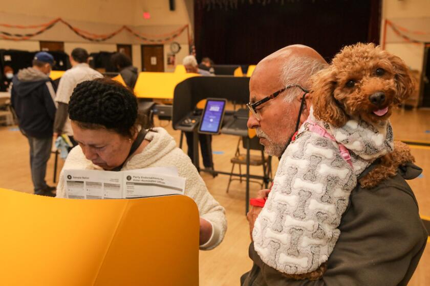 Los Angeles, CA - November 08: Fidel Flores, 67, holds dog Lulu as his wife Anna Marina Flores, 67, works on her ballot at polling station at Boyle Heights Senior Center on Tuesday, Nov. 8, 2022 in Los Angeles, CA. (Irfan Khan / Los Angeles Times)
