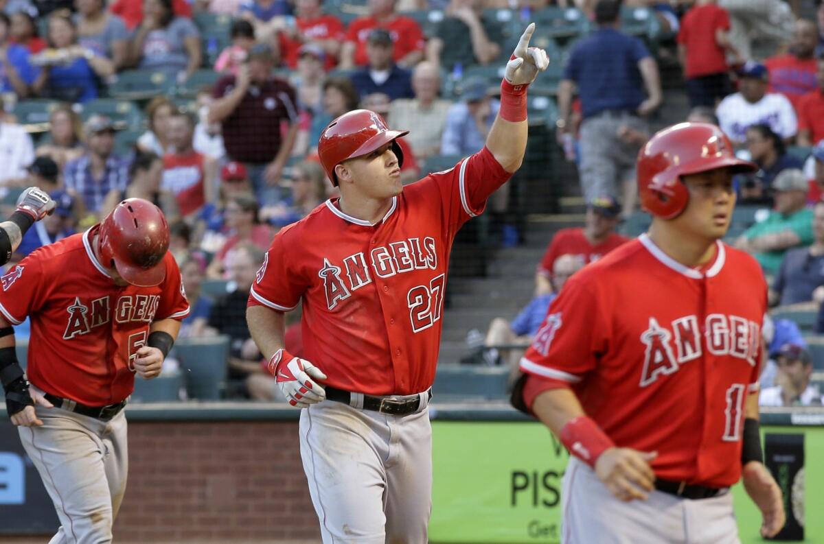 Mike Trout points to the stands after hitting a three-run home run off of Texas' Colby Lewis to score Kole Calhoun, left, and Hank Conger, right, in the second inning. The Angels defeated the Rangers, 15-6.