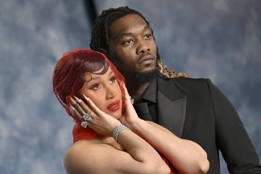 Cardi B in a red dress and matching red veil covering her face posing next to Offset in a black suit