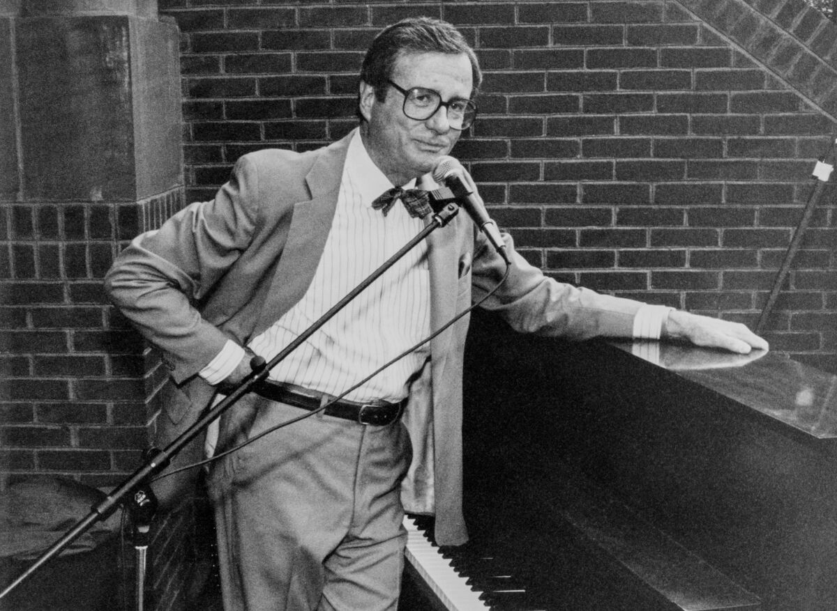Mark Russell standing beside a piano and in front of a microphone.