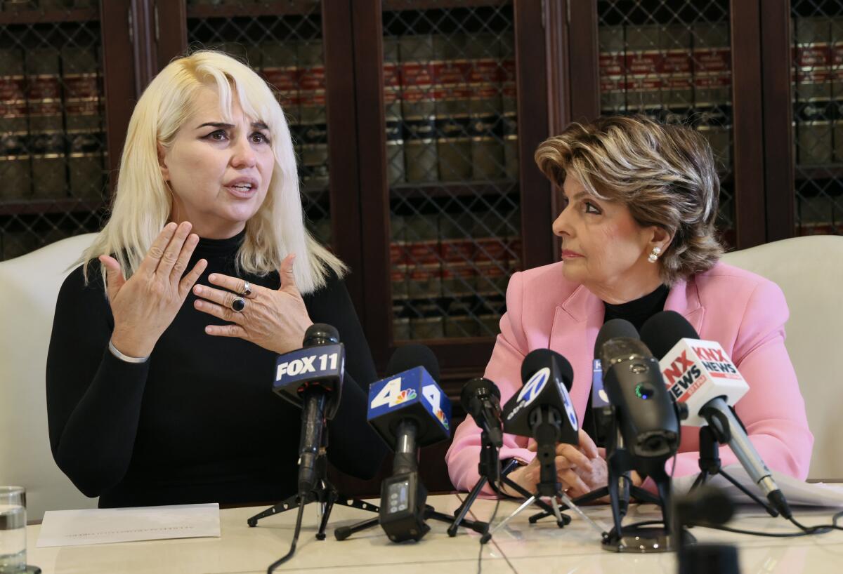 Two women sit behind a table with several microphones on it.