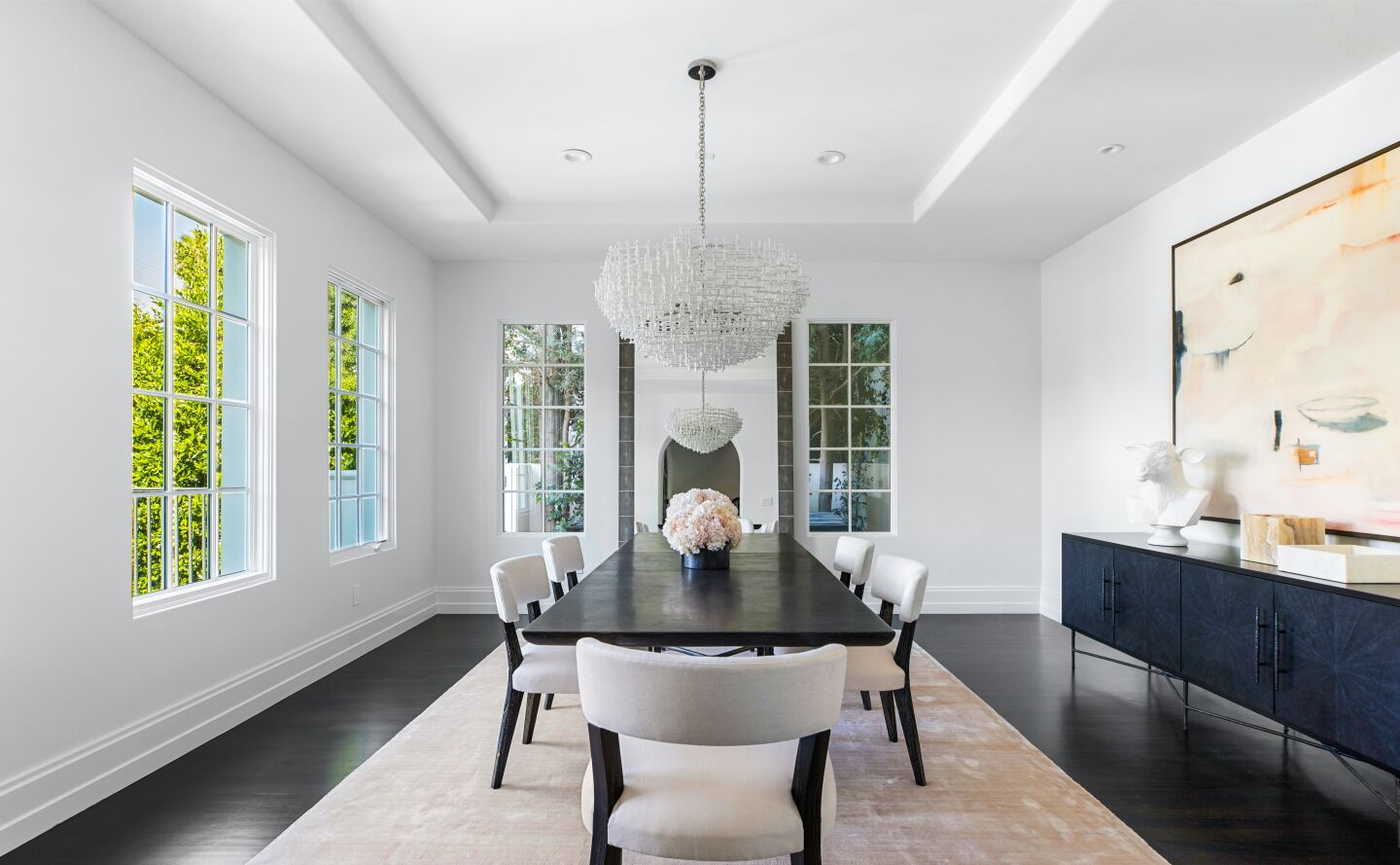 White walled dining room with dining furniture, art, dark wood floors and windows overlooking greenery.