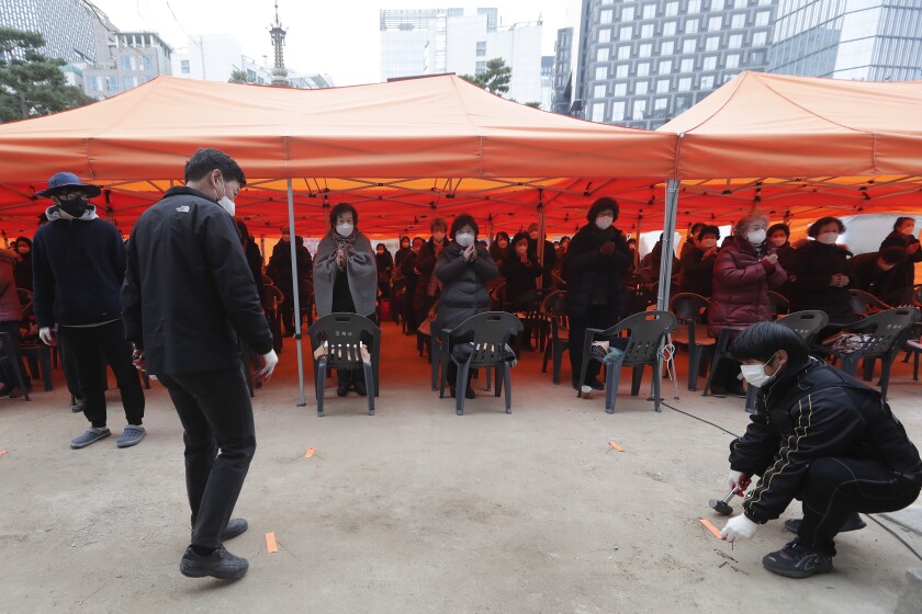 Workers mark social distancing signs as parents wearing face masks pray during a service to wish for their children's success on the eve of the college entrance exam at the Jogyesa Buddhist temple in Seoul, South Korea, Wednesday, Dec. 2, 2020. About 490,000 high school seniors and graduates across the country are expected to take the College Scholastic Ability Test. (AP Photo/Ahn Young-joon)