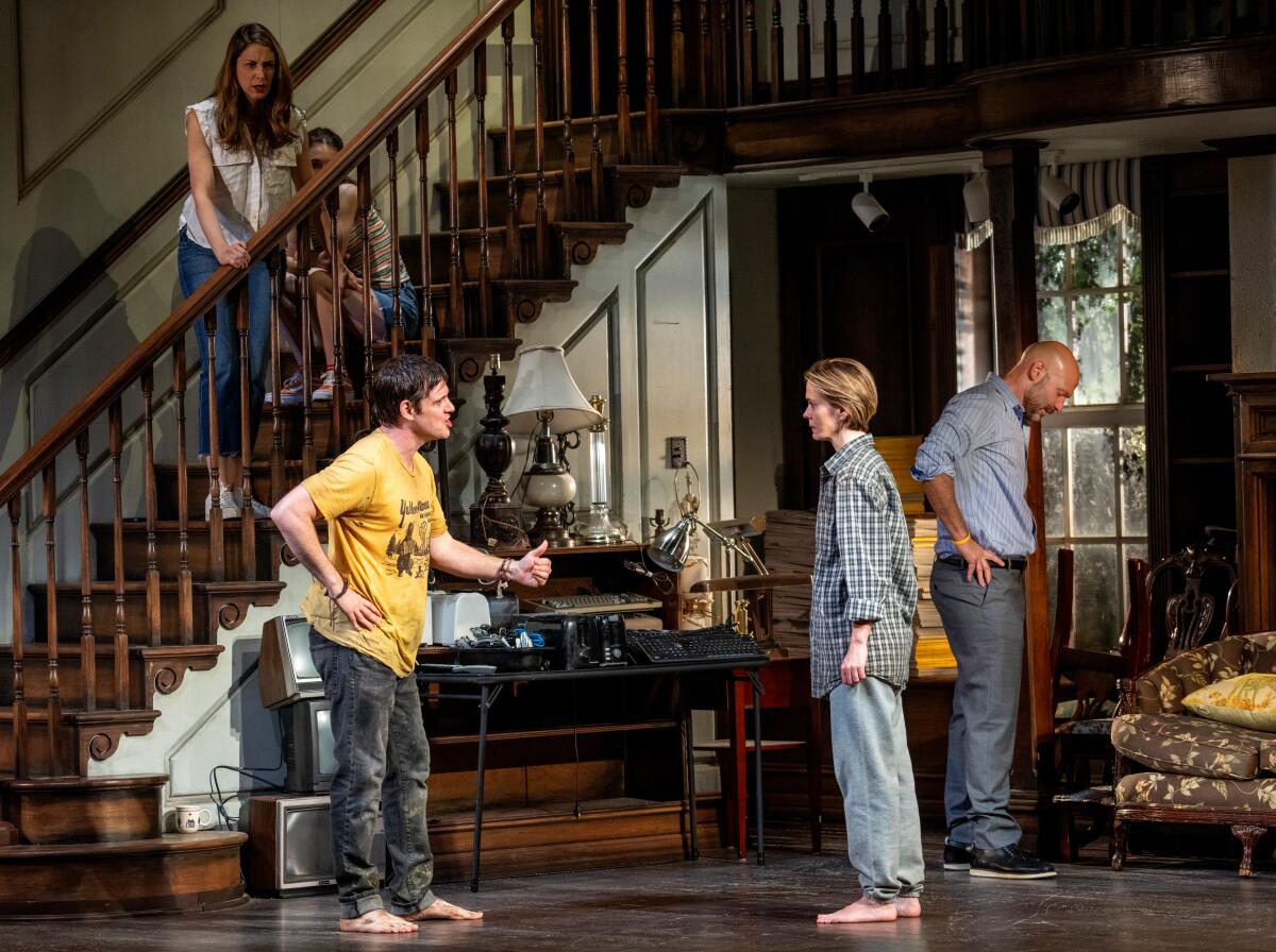 People standing in a living room and on the stairs at one side of it on a stage set