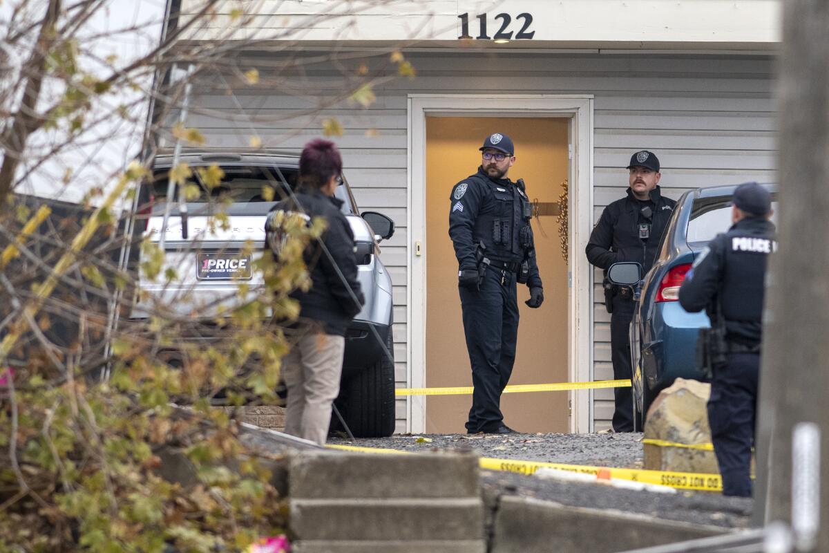 Investigators stand outside the door of a home surrounded by police tape