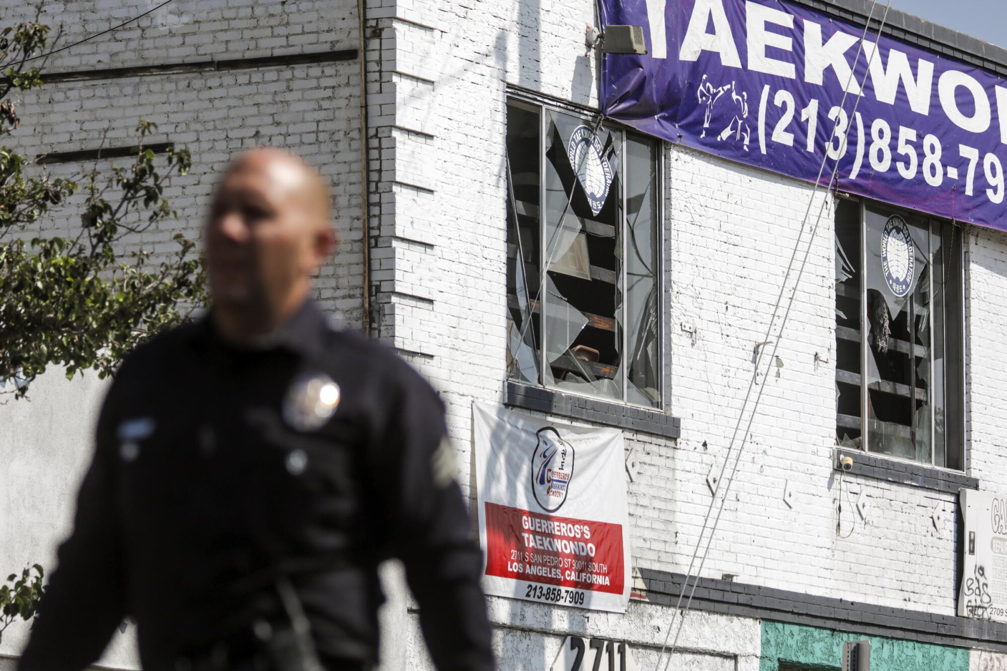 A police officer is seen in front of a building with shattered windows.