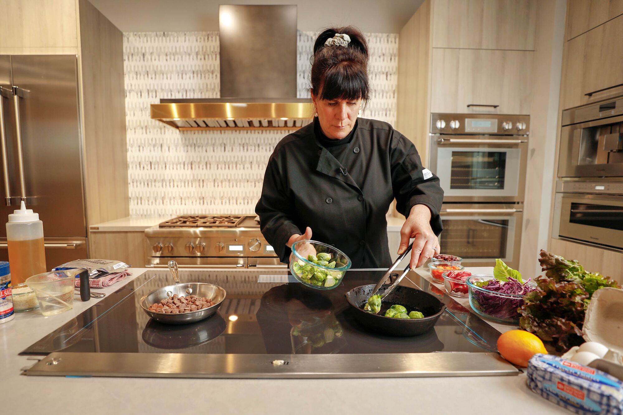 Bridget Bueche uses tongs to move Brussels sprouts in a pan on an induction cooktop. 