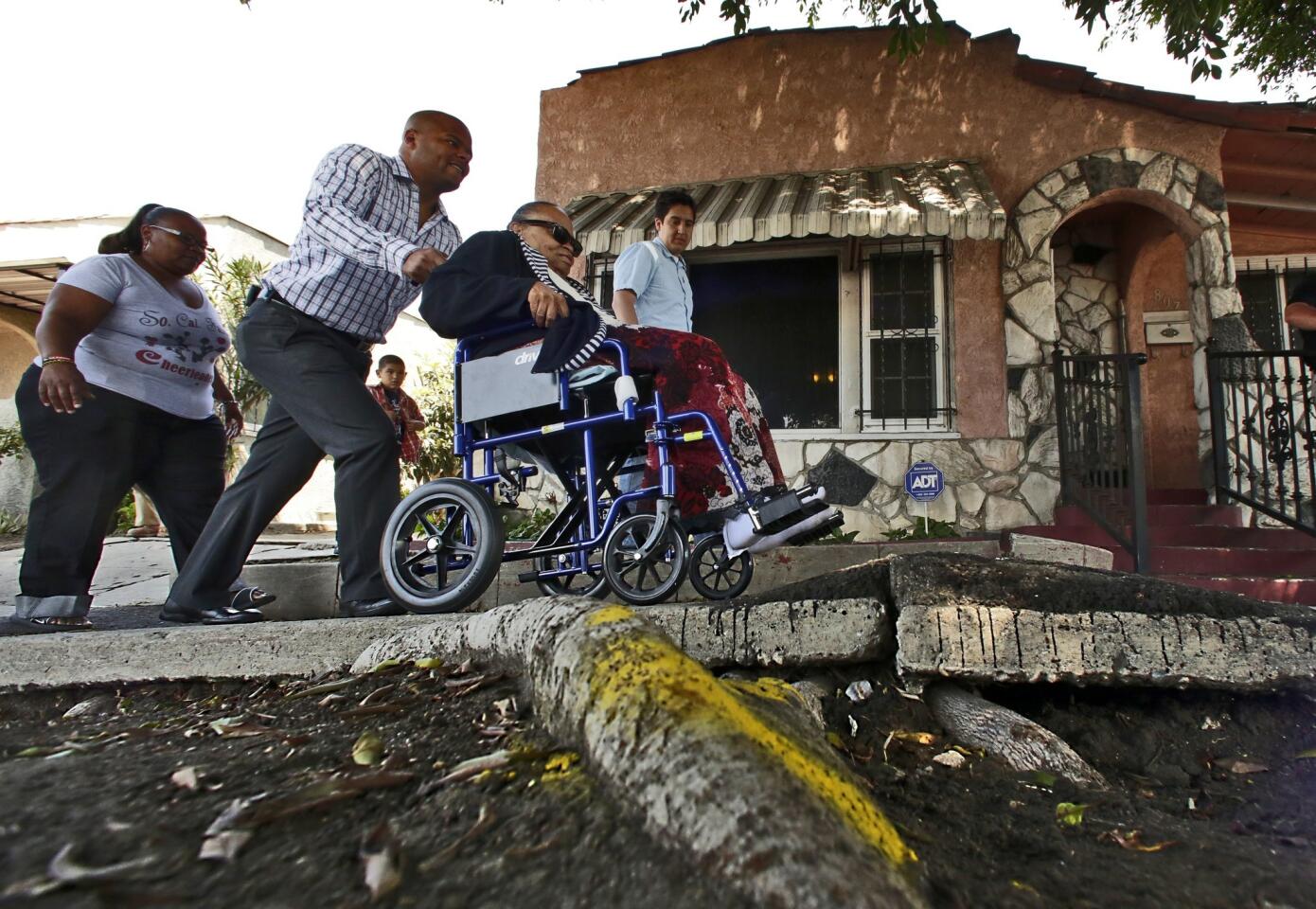Bernard Parks Jr., chief of staff of Councilman Bernard Parks, pushes Helen Young, 80, in a wheelchair over a broken sidewalk in front her home on West Century Boulevard in Los Angeles, where Councilman Parks and the L.A. Neighborhood Initiative marked the start of several sidewalk repair projects.
