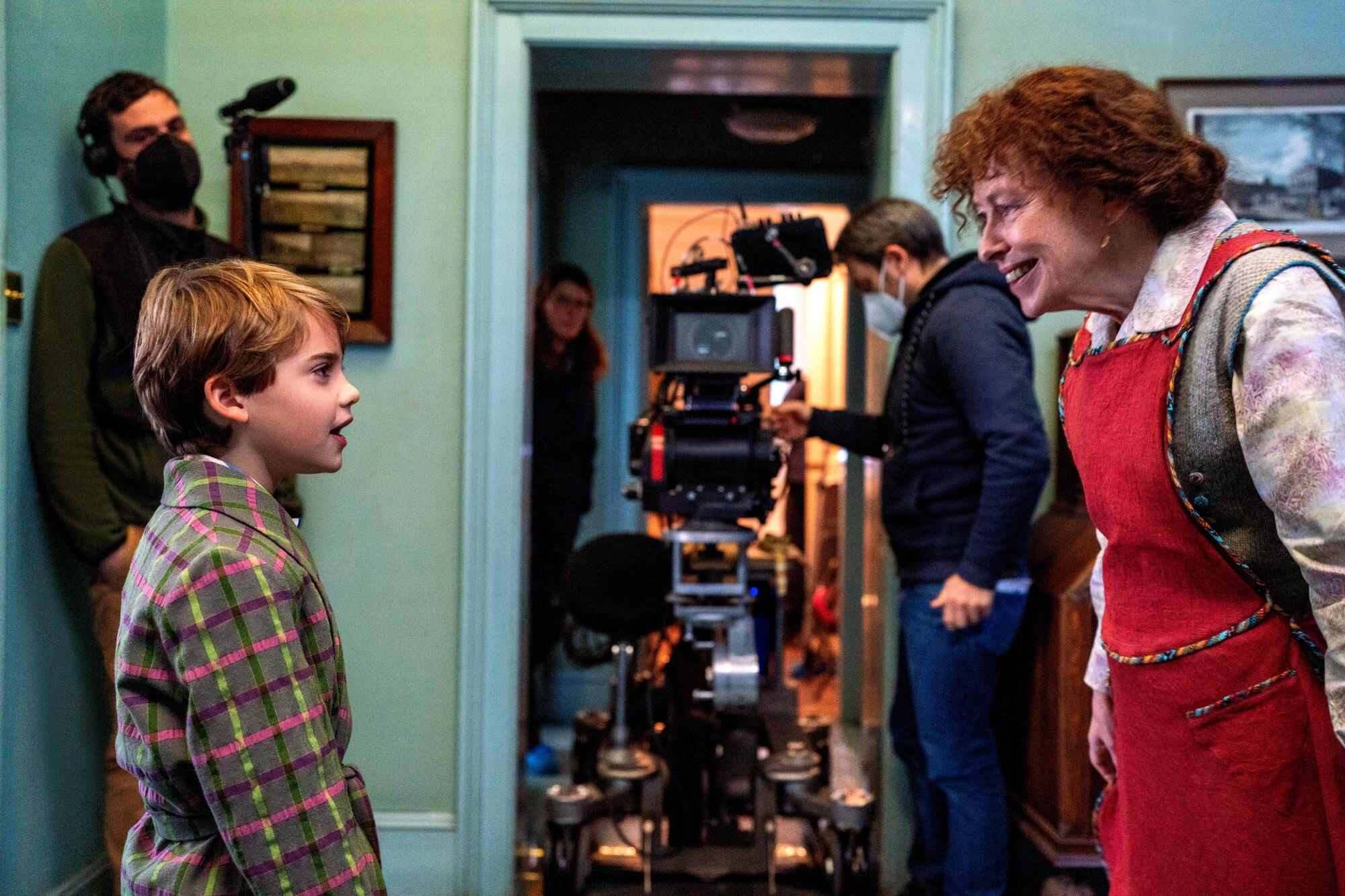 A boy looks at a woman on a set with cameras and production staff looking at them.