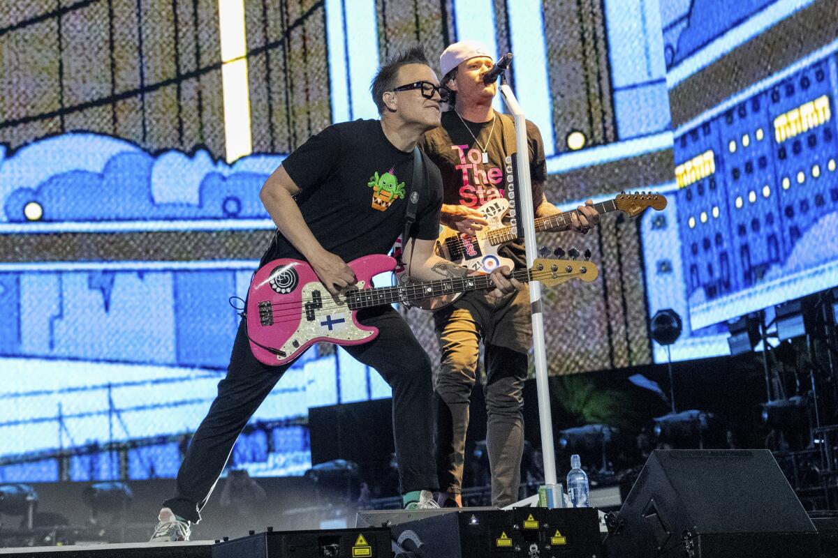 Mark Hoppus and Tom DeLonge holding guitars and singing into the same mic while performing on stage