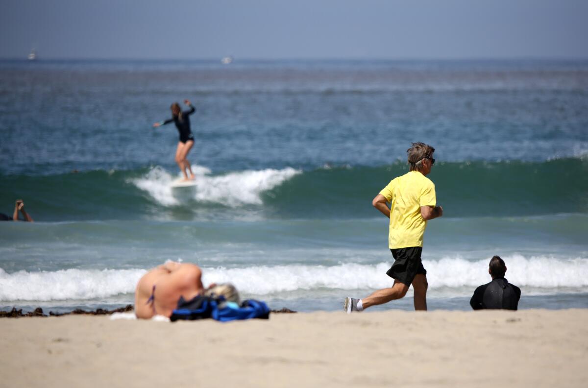 One day after Newport Beach opened up its beaches to recreational activities, surfers and joggers took to the shore at the Newport Pier in Newport Beach on Thursday.