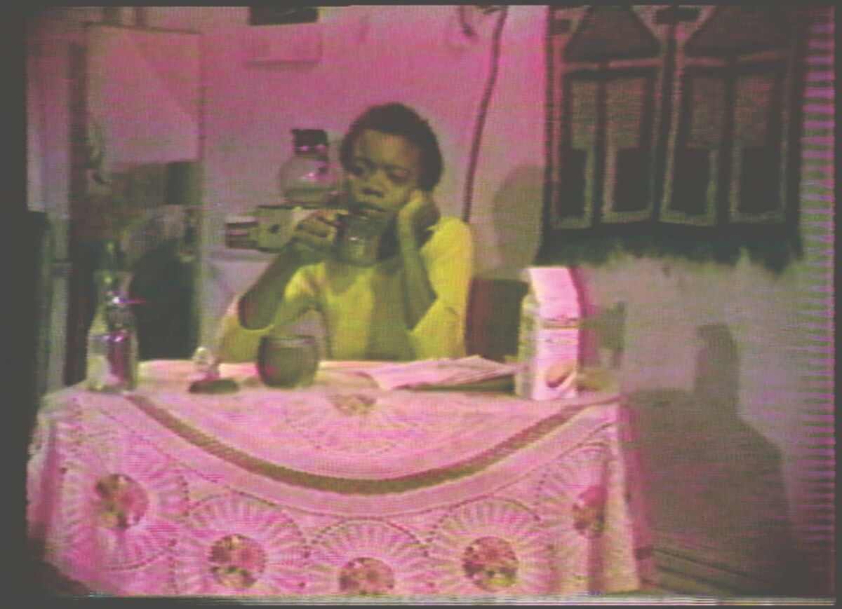 A woman sits at a table in a video still from "Cycle," 1978.