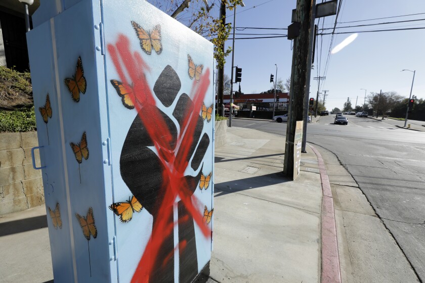 A large red X is sprayed over the fist on the mural.