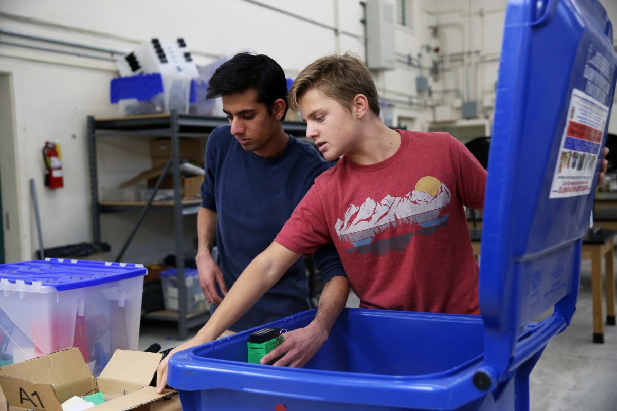 Akshat Bansal, 17, left, and William Bacon, 16, demonstrate a work in progress to minimize trash from blowing out from bins in their communities.
