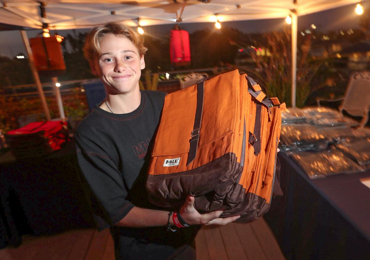 Event coordinator Hero Glowaki holds popular backpacks during a pop-up event of Nalu clothing on Monday night in Seal Beach.