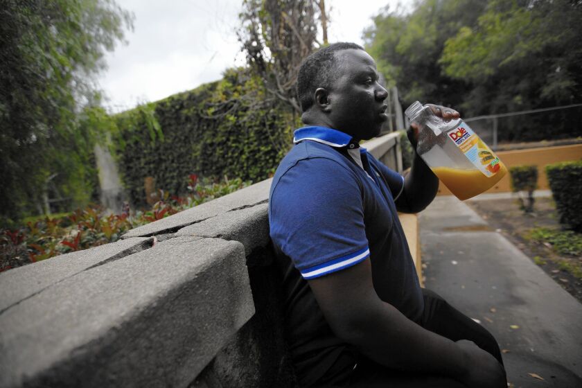 Musa Kalawa drinks juice on a walkway at the St. Andrews Garden apartments across the wall from the Freeport-McMoRan Oil and Gas drilling site in South L.A. Residents are concerned about oil fumes and possible expansion at the business.