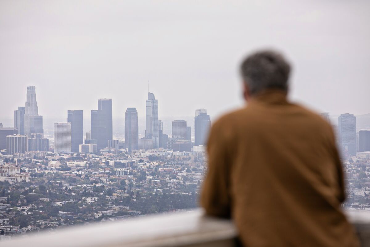 A man enjoys a view of the downtown Los Angeles skyline on an overcast day at Griffith Observatory.