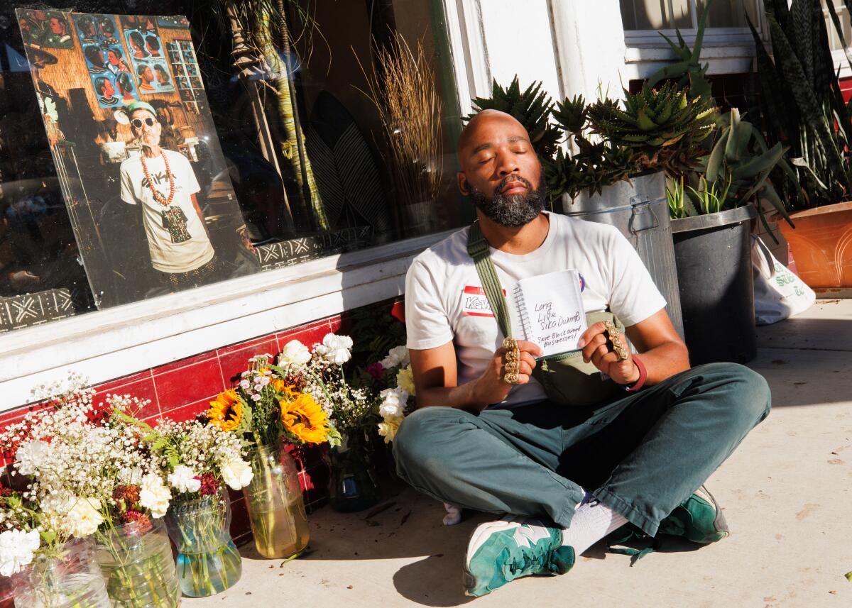 A photo of a man sitting outside next to a memorial of Sika Dwimfo during his vow of silence.