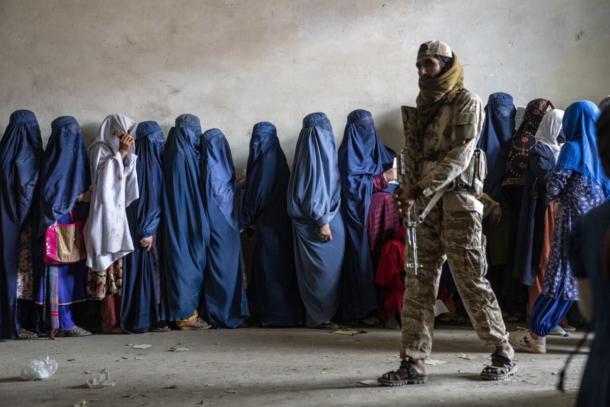 A Taliban fighter stands guard oven a line of women wearing burqas. 