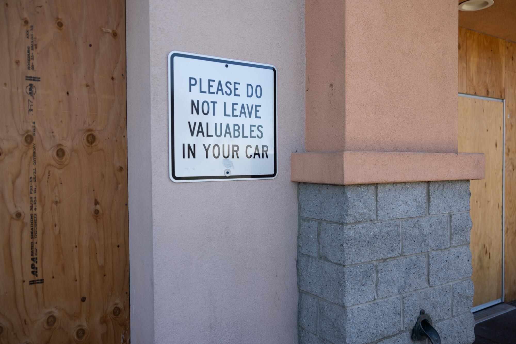The outside of a boarded-up building, with a sign on the wall reading "Please do not leave valuables in your car."