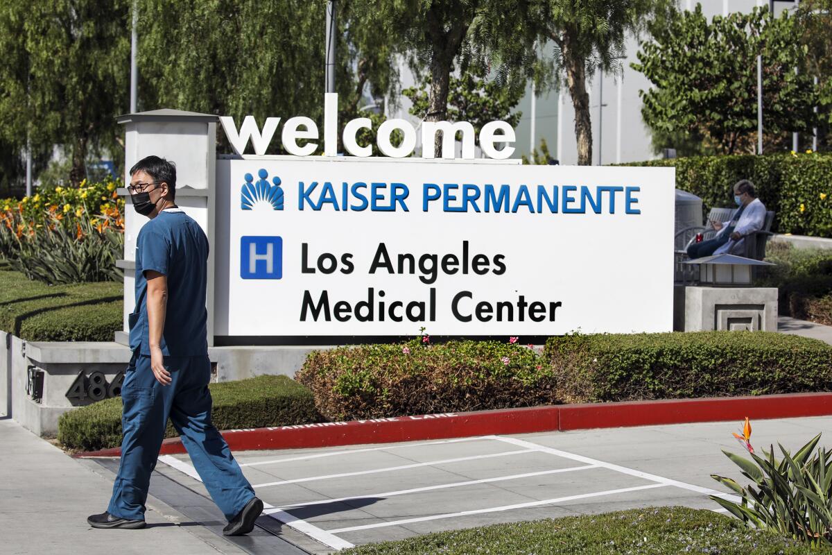 A man in scrubs and a mask walks in front of a welcome sign for Kaiser Permanente Los Angeles Medical Center