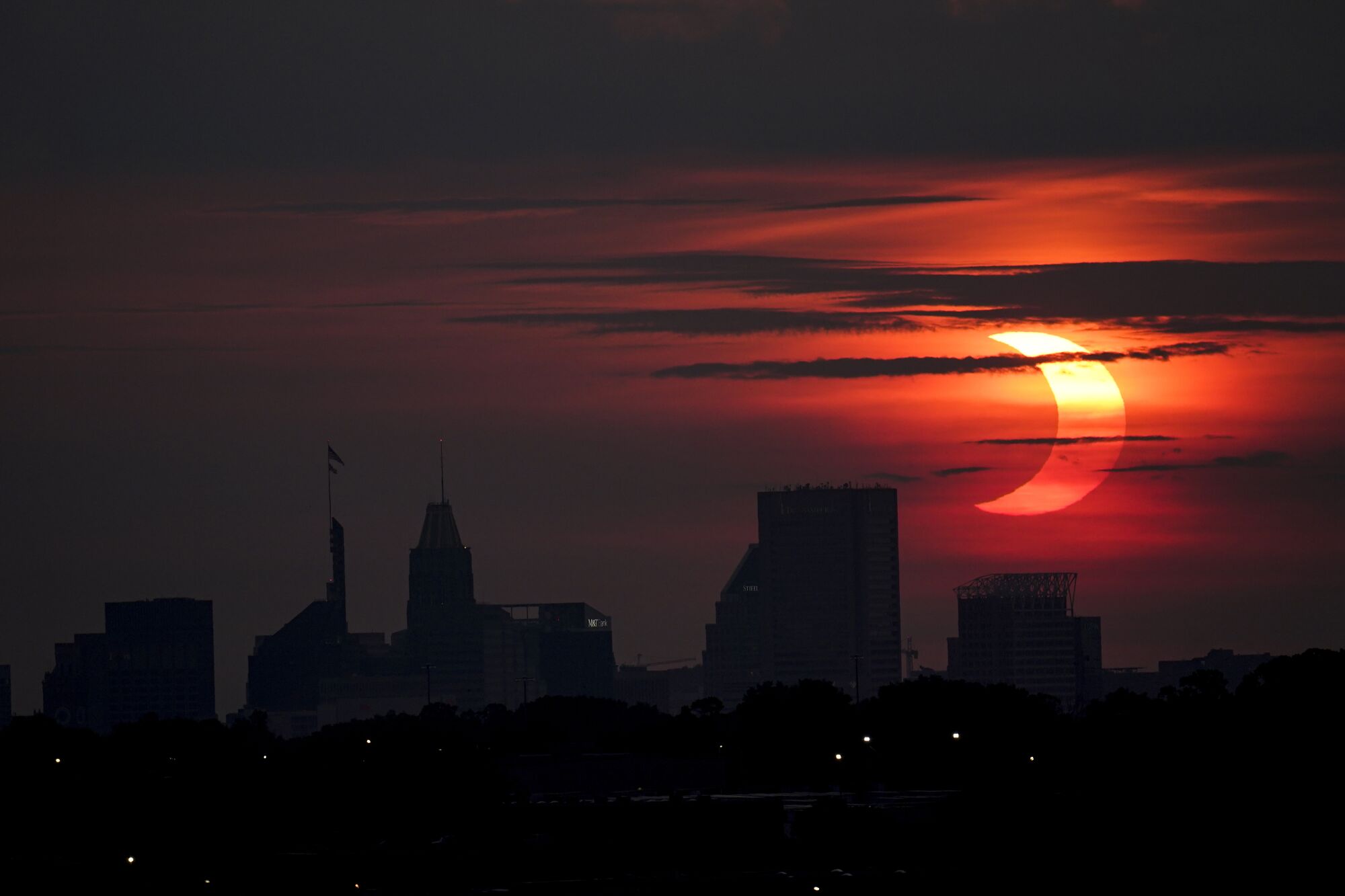 A partial solar eclipse rises over the Baltimore skyline, as seen from Arbutus, Md.