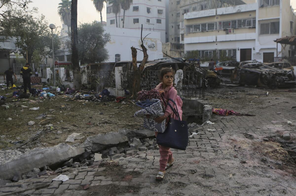 Una niña cargando mantas pasa frente al hospital al-Ahli, destruido por una explosión, en Ciudad Gaza,