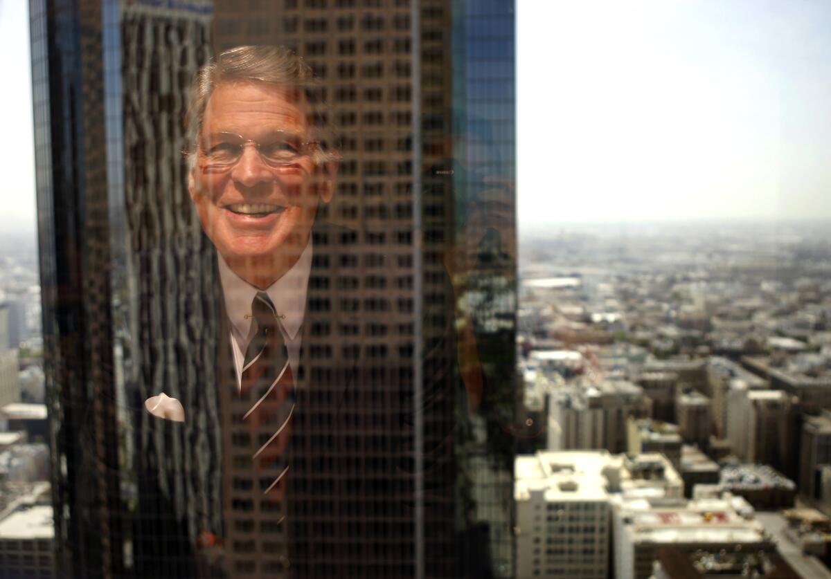 A man in a suit is reflected in a window overlooking downtown L.A.
