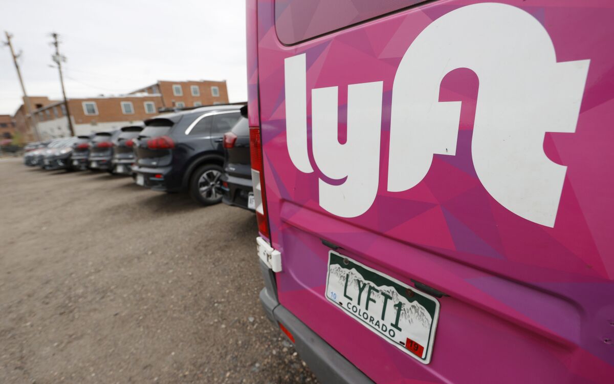 FILE - In this April 30, 2020, file photo, Kia Neros that are part of the Lyft ride-hailing fleet sit unused in a lot near Empower Field at Mile High in Denver. Lyft says it’s adding a fuel surcharge of 55 cents to each ride its drivers perform to help offset recent gasoline price increases. The company said in a blog post on Wednesday, March 16, 2022, that the surcharge will be effective beginning next week, with all of the money going directly from riders to its drivers. (AP Photo/David Zalubowski, File)