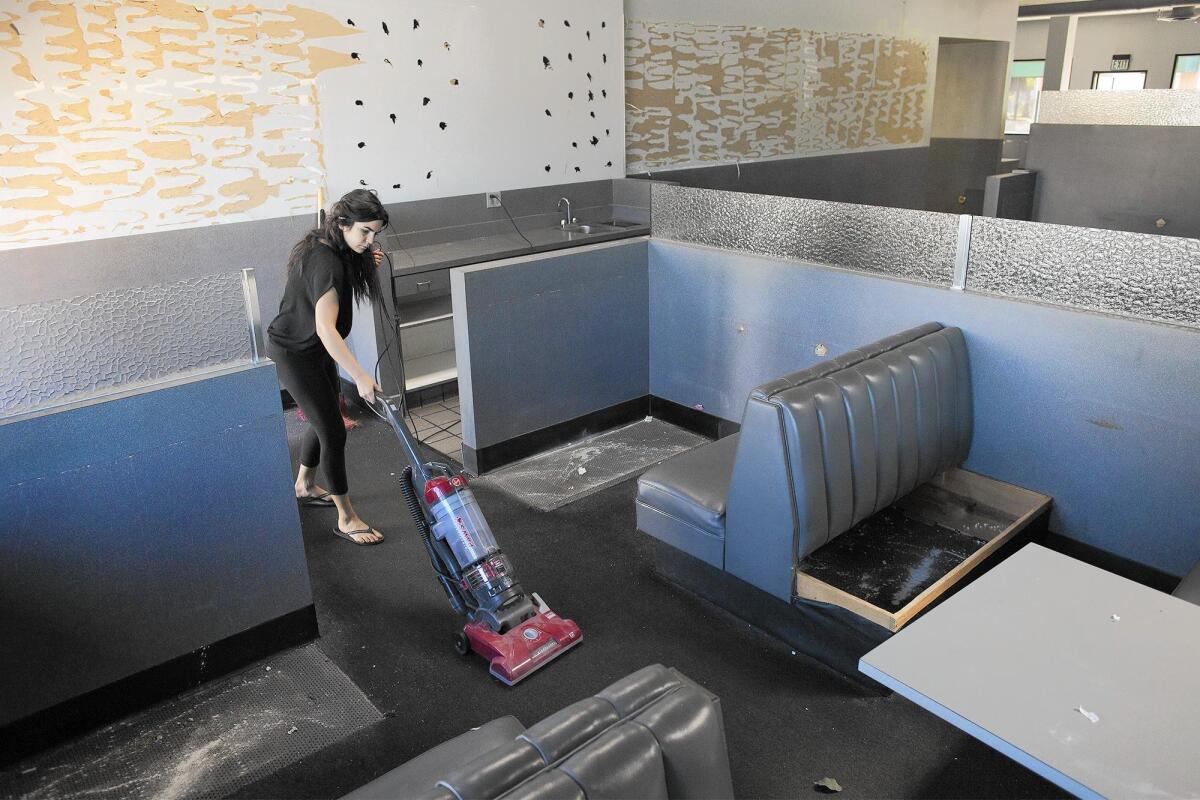 SueAnn Challita vacuums an eating area as her family officially closes Arnie's Manhattan Restaurant and Deli in Newport Beach on Friday.