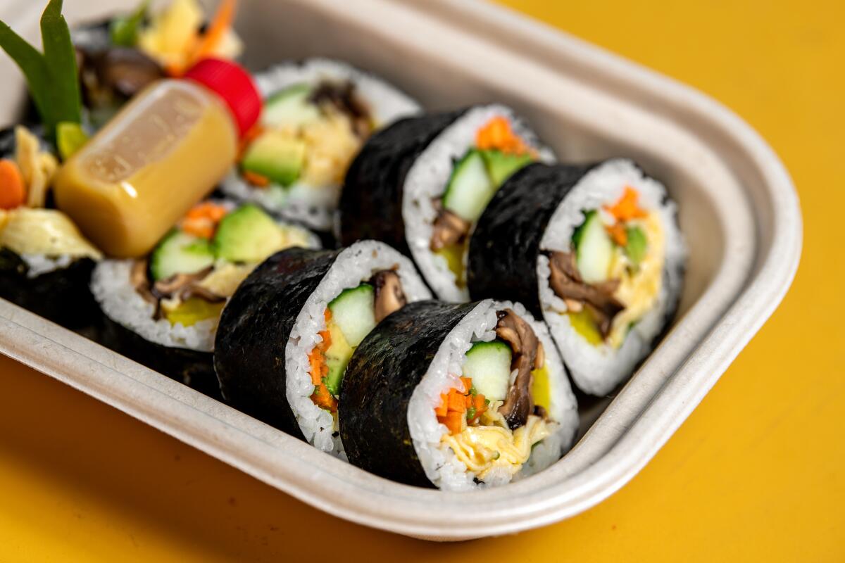 Slices of gimbap in a takeout container with a little bottle of sauce