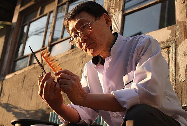 Lee Nam-yul sits outside his rickety barber shop in Seoul to examine his tools in brighter light. He prefers to cut hair using the same implements his grandfather did.