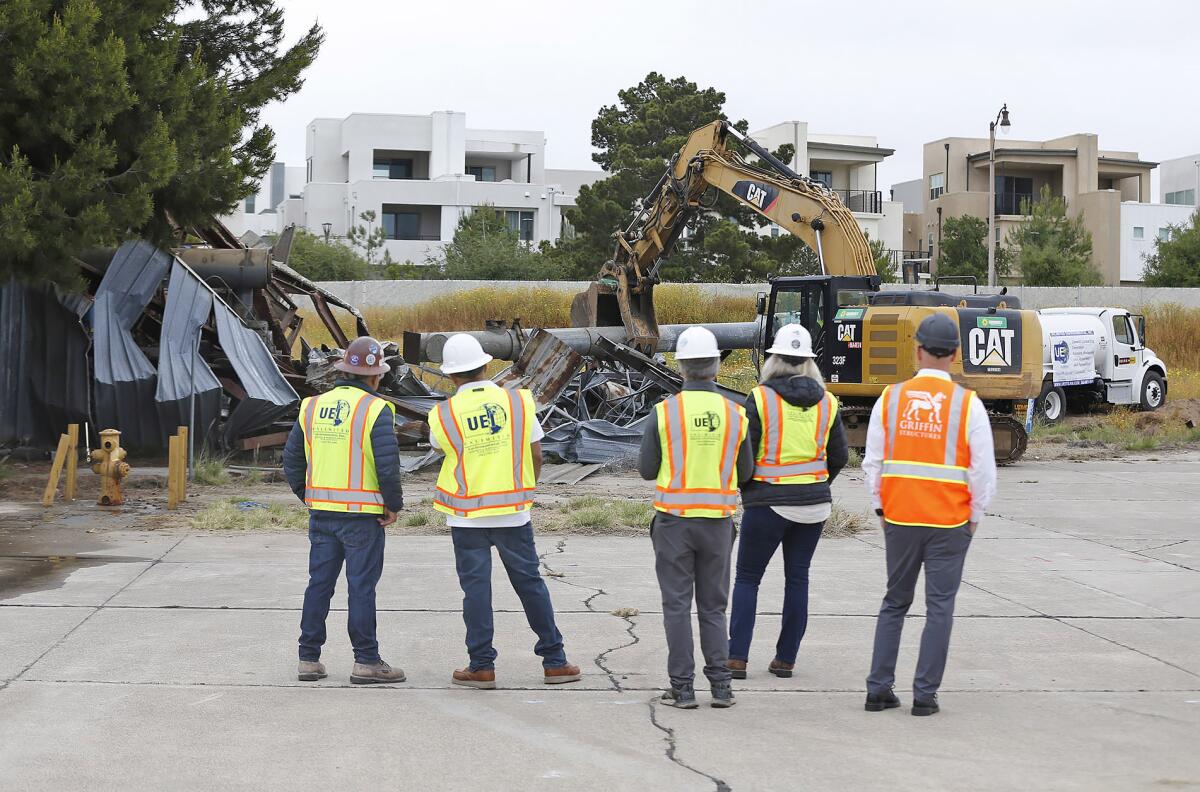 Crew members watch as their excavator demolishes an old military structure on Tuesday at the Great Park in Irvine.