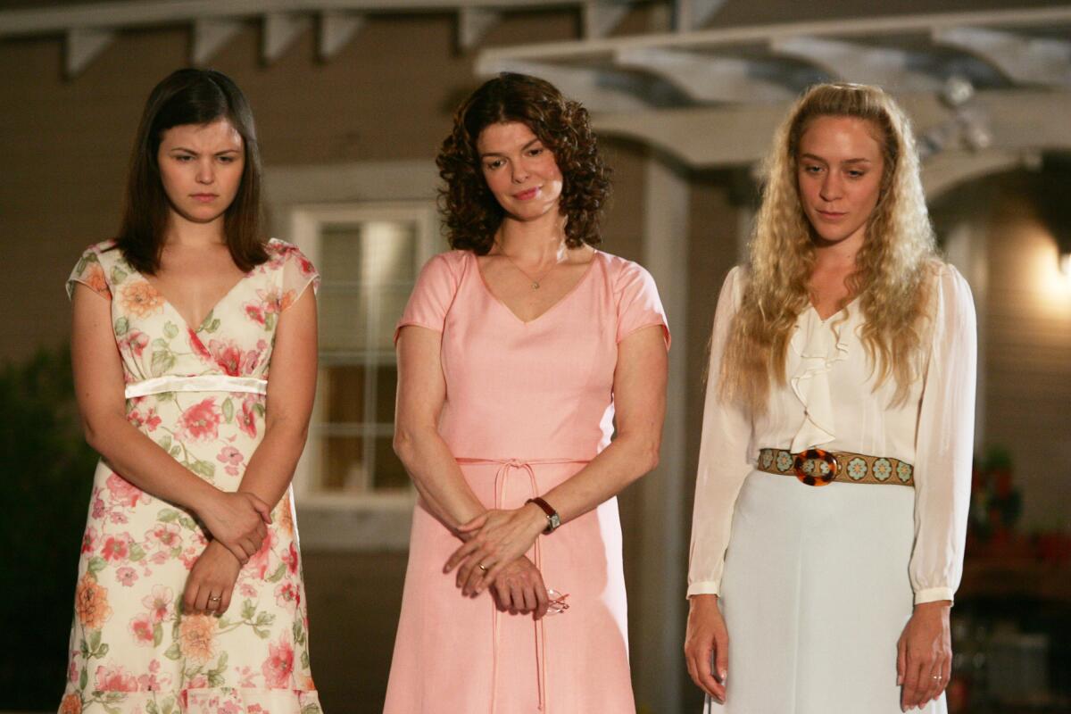 Three women standing in front of a house look down.