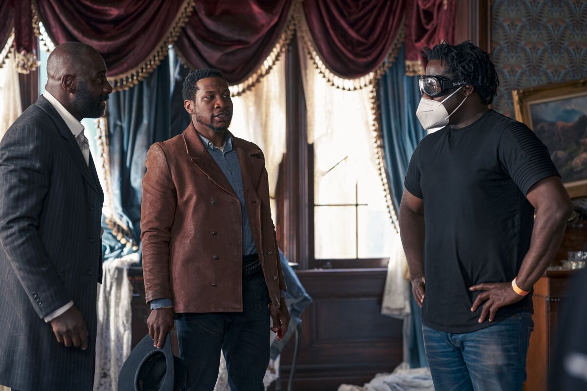 From left, Idris Elba as Rufus Buck and Jonathan Majors as Nat Love with writer-director Jeymes Samuel in an ornate room
