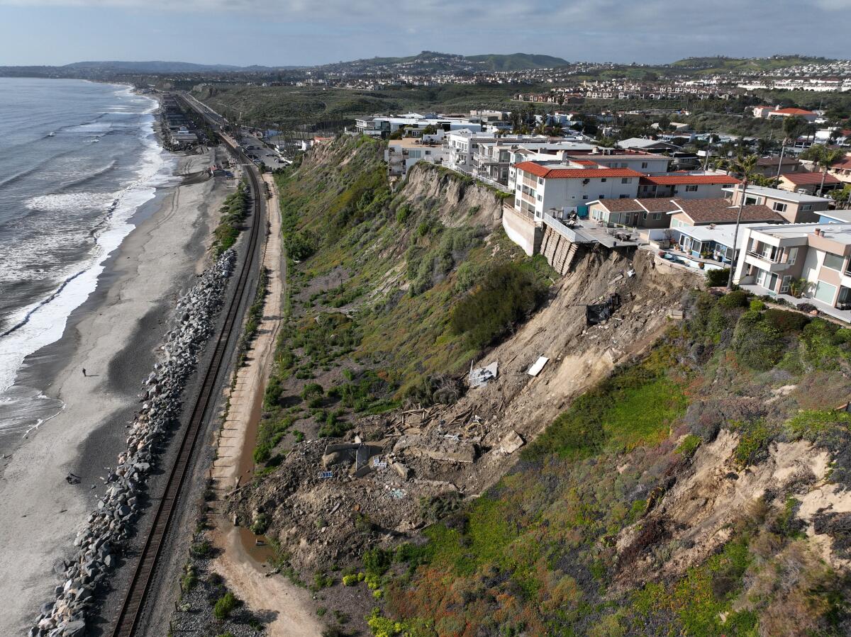 Aerial view of landslide, with backyards of multiple residential buildings collapsing down a hillside toward the beach below
