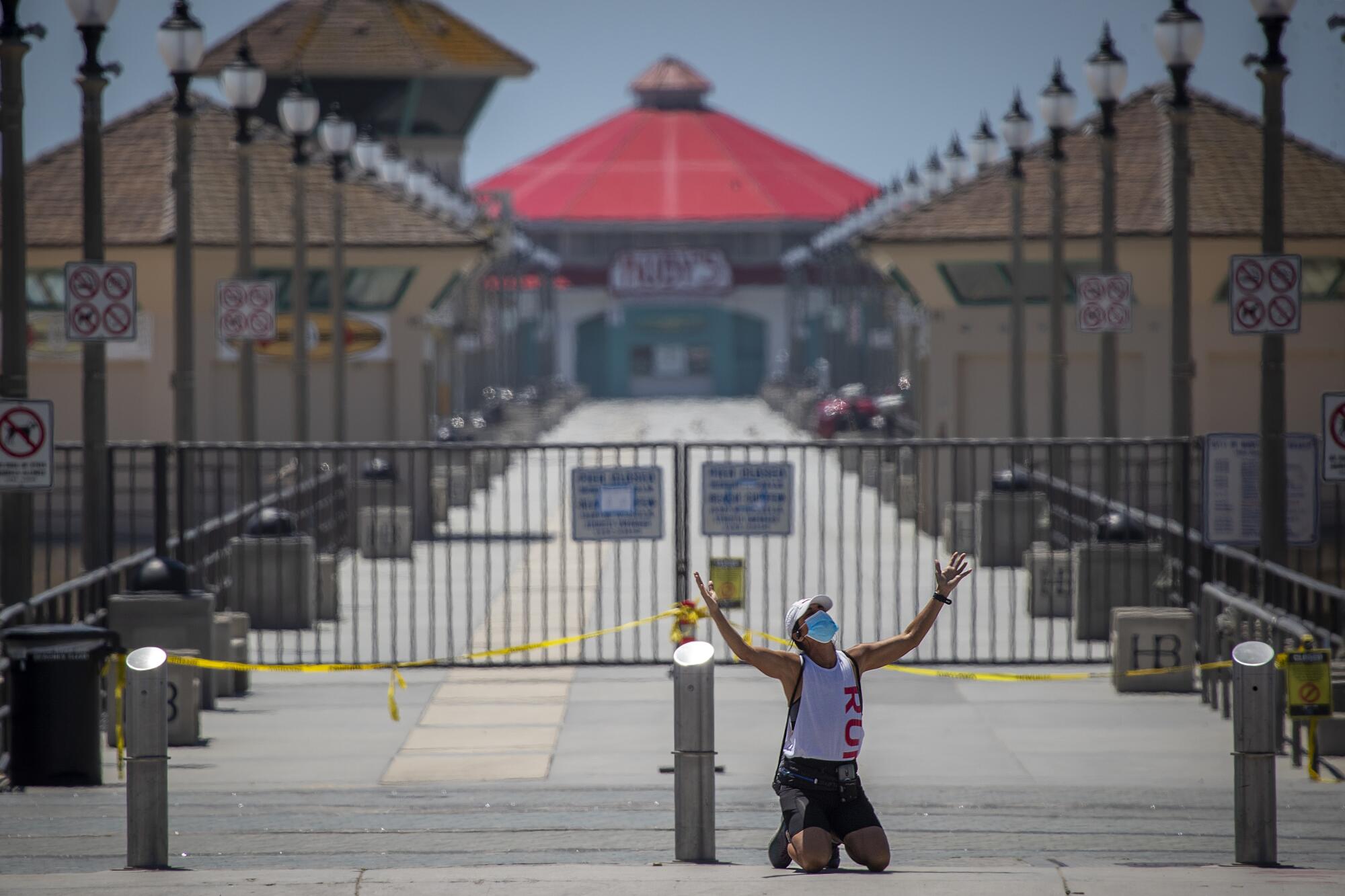 A woman kneels with her arms outstretched to the sky in front of caution tape and closed gates at a pier