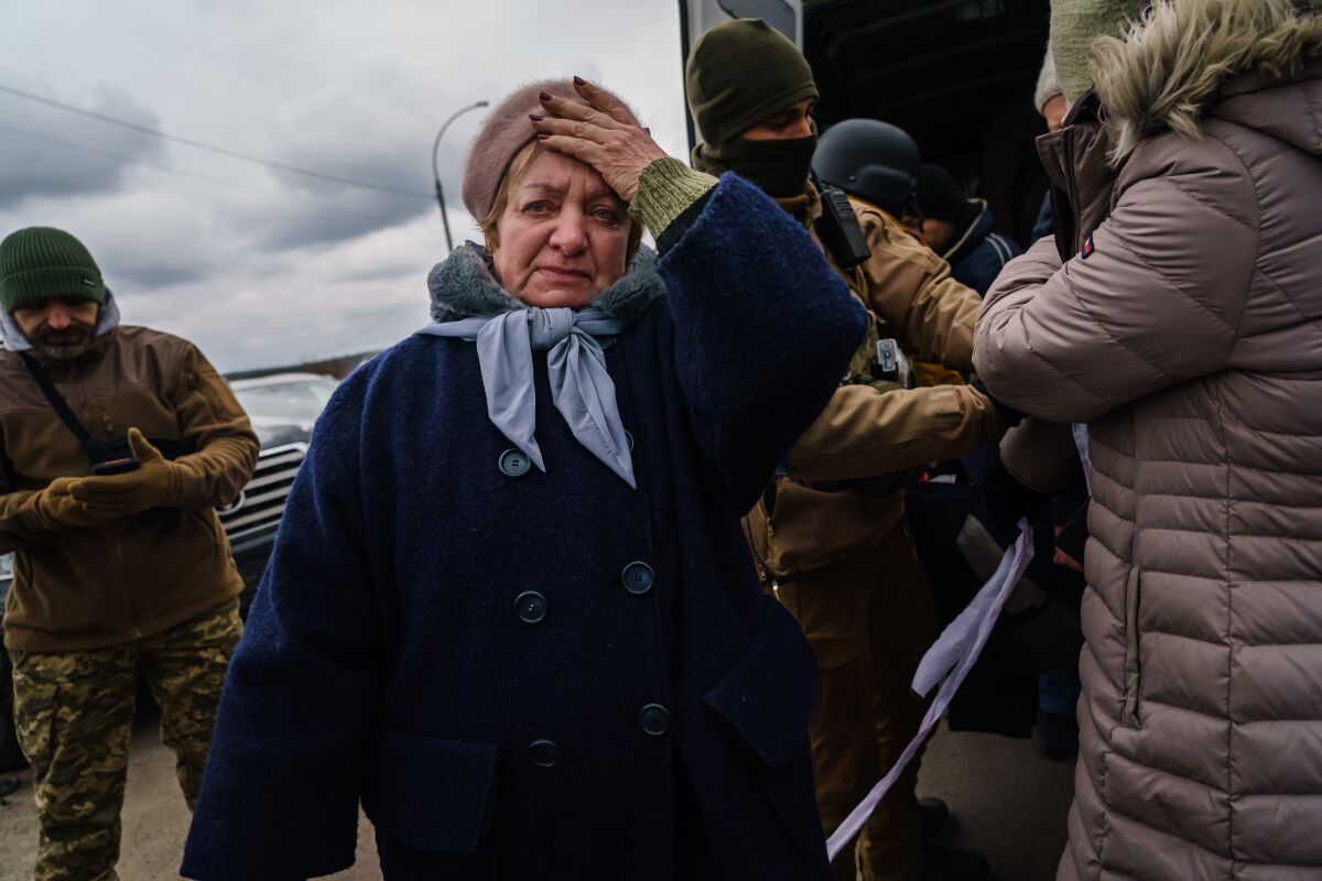 A woman in a blue coat holds her hand to her head near men in military fatigues