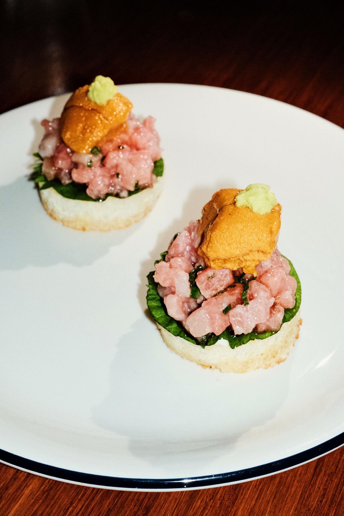 Two circular pieces of bread topped with uni, wasabi and chopped raw tuna on a white plate at Japanese-French bistro Camélia