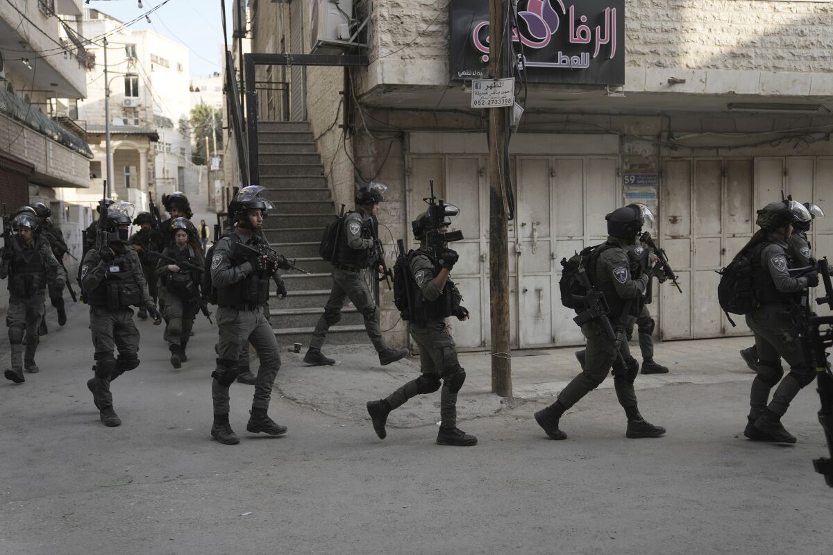 A group of armed uniformed personnel walk down a street