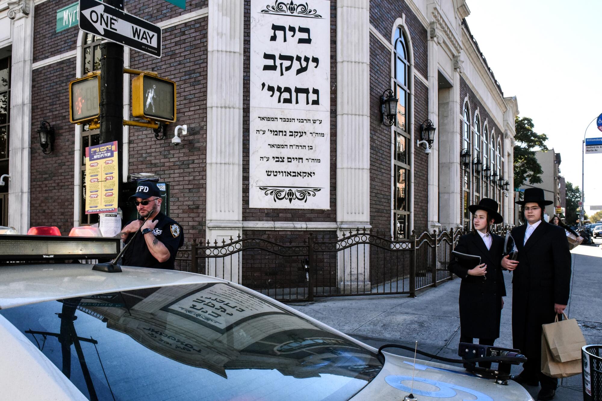 A police officer on a street corner near two men in ultra-Orthodox Jewish attire.