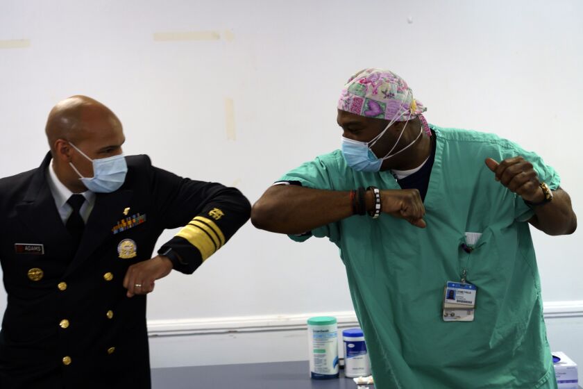 Surgeon General of the U.S. Jerome Adams, left, elbow-bumps Emergency Room technician Demetrius Mcalister after Mcalister got the Pfizer COVID-19 vaccination at Saint Anthony Hospital in Chicago, on Tuesday, Dec. 22, 2020. (Youngrae Kim/Chicago Tribune via AP, Pool)