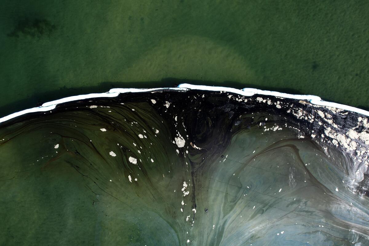 An aerial photo shows floating barriers known as booms holding back oil