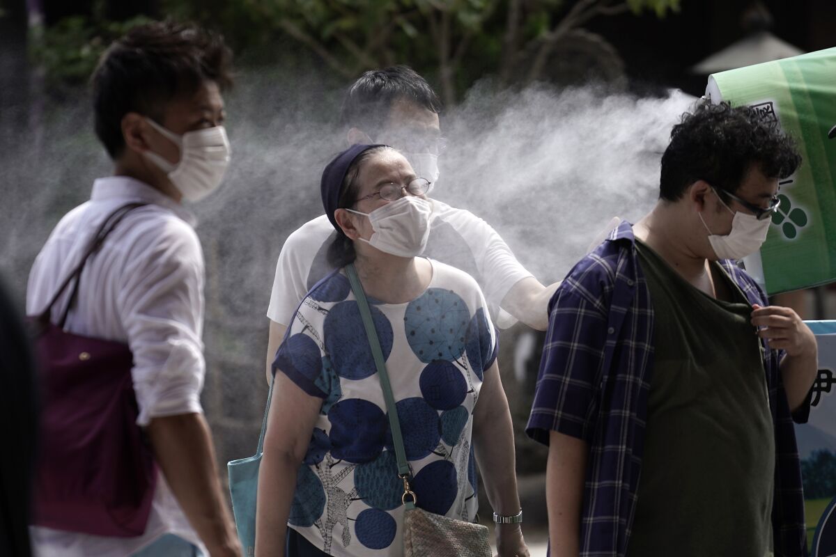 A woman wearing a protective mask to help curb the spread of the coronavirus cools down under a cooling mist spot at in Asakusa district Friday, Aug. 14, 2020, in Tokyo. The Japanese capital confirmed more than 380 coronavirus cases on Friday. (AP Photo/Eugene Hoshiko)