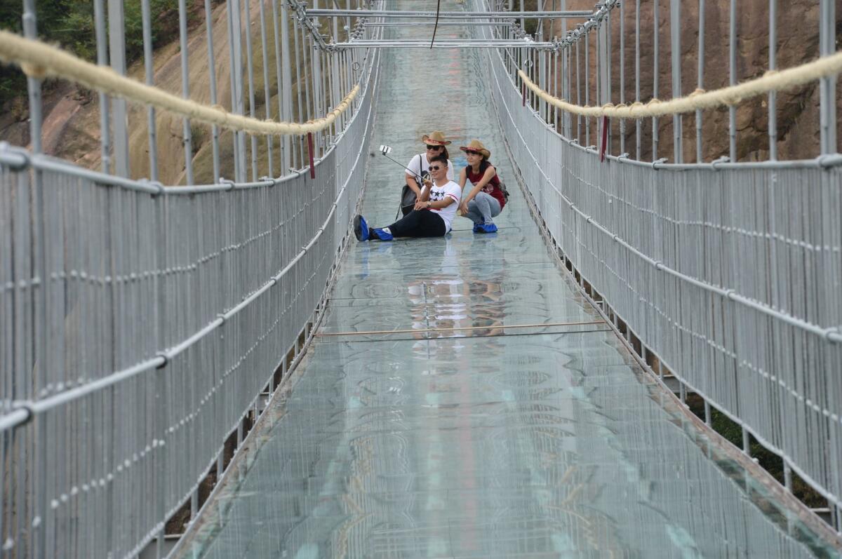 Tourists take a selfie on a suspension bridge made of glass at the Shiniuzhai National Geological Park.