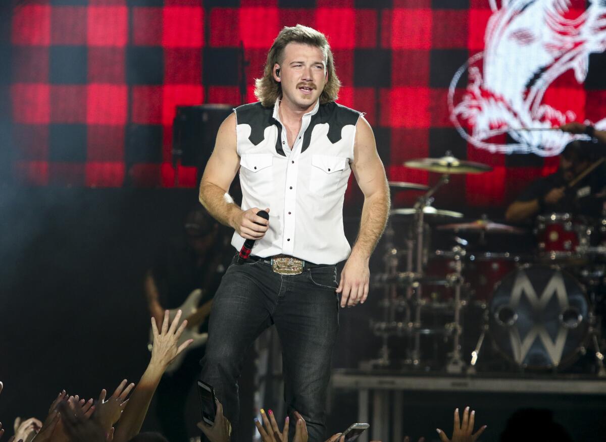 A man with a mullet hairstyle wearing a vest performs onstage.